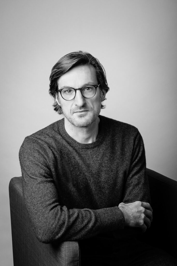 Portrait professionnel en studio : homme en pull et lunettes sur fond gris neutre